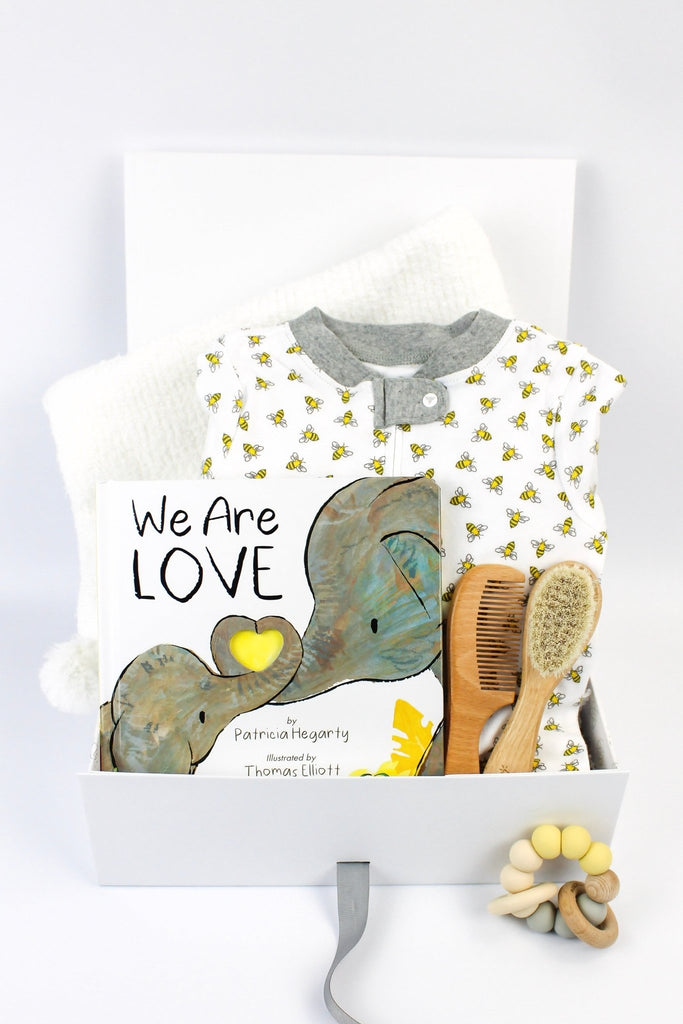 A baby gift box featuring a cotton onesie, a board book, a blanket, a wood and brush set plus teether.