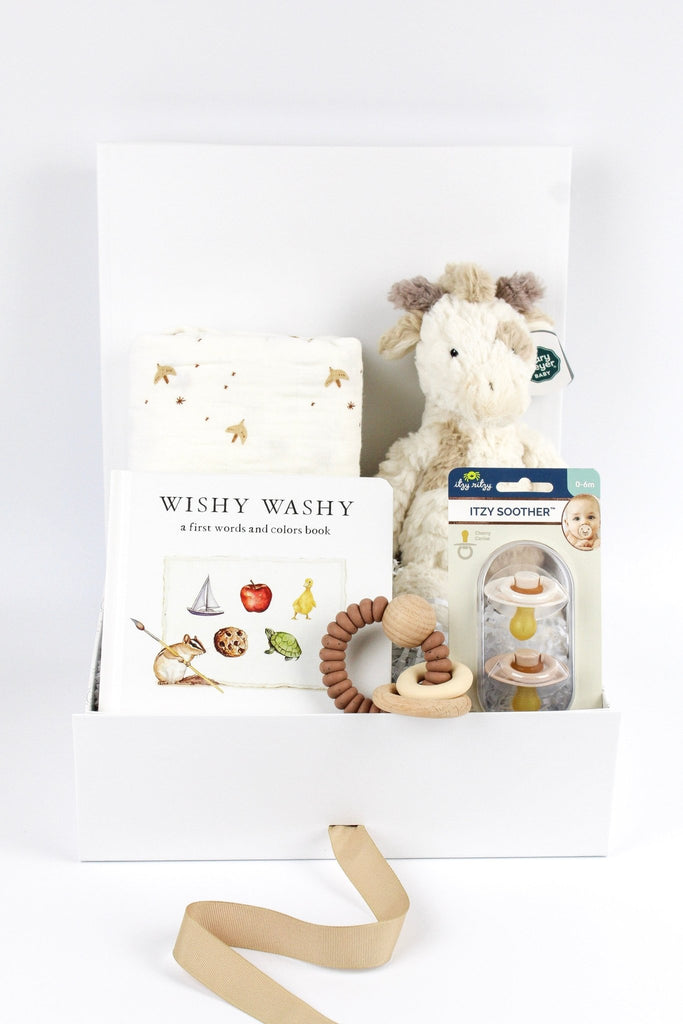 A timeless and classic neutral baby gift box featuring an organic cotton swaddle, a giraffe toy, a board book, pacifiers and a teether for a new baby.
